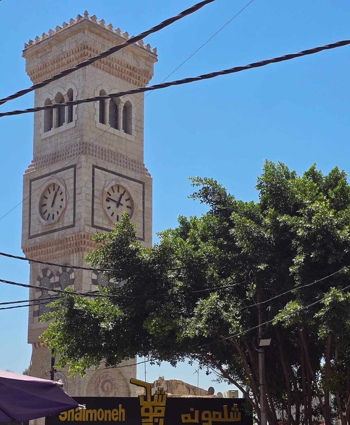 برج الساعة في وسط مدينة إربد بين الأشجار تحت سماء زرقاء صافية